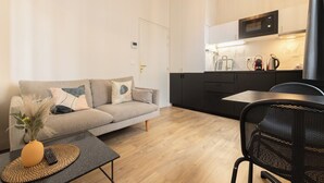 A modern apartment with a sofa, a dining table, a kitchen with a microwave, and a black chair. - Beautiful renovated apartment for 2 in front of the Gare Saint-Jean (Bordeaux)