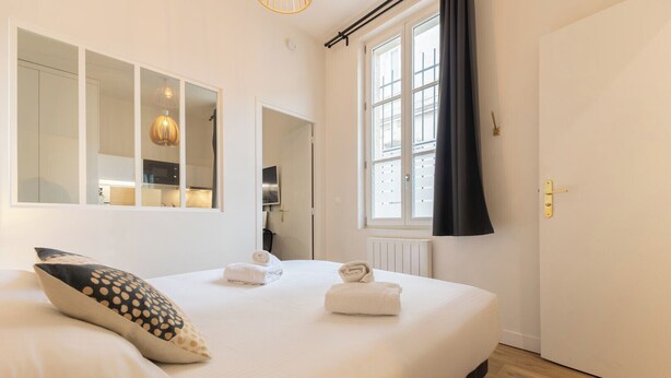 A bedroom with a bed, a mirror, a window with curtains, and a door. - Beautiful renovated apartment for 2 in front of the Gare Saint-Jean (Bordeaux)