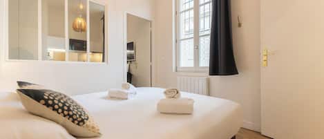 A bedroom with a bed, a mirror, a window with curtains, and a door.