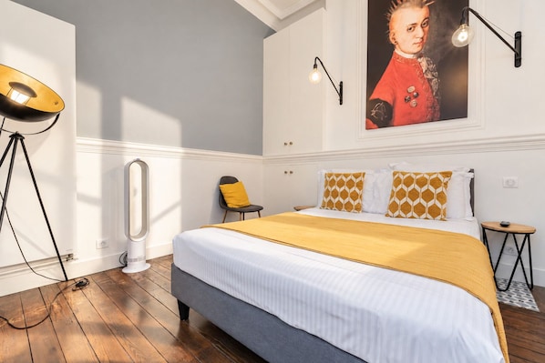 A bedroom with a large bed, a standing lamp, a chair, and a wall-mounted picture.