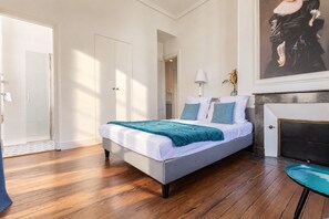 A bedroom with a bed, a door, a lamp, and a painting.