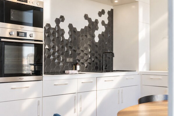 A modern kitchen with a built-in oven, a stainless steel range hood, and a hexagonal backsplash.