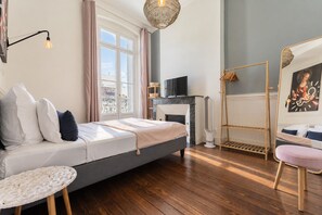 A bedroom with a bed, a TV, a fireplace, a chair, and a window with curtains.
