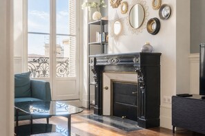 A living room with a fireplace, a glass coffee table, a blue sofa, and a television.