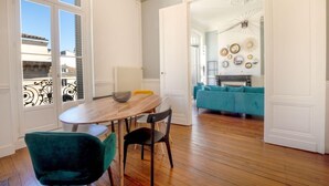 Un comedor con una mesa y sillas de madera, un tazón sobre la mesa y un sofá color azul verdoso al fondo.