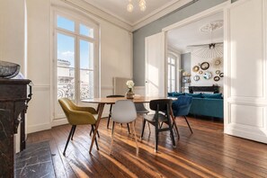 Un coin repas avec une table et des chaises en bois, une vue par la fenêtre et un canapé bleu en arrière-plan.