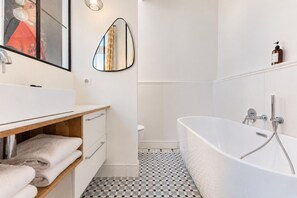 A bathroom with a bathtub, a toilet, a sink with a mirror, and a towel rack.