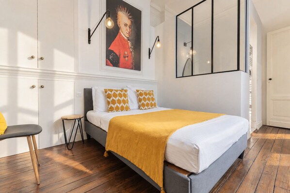 Une chambre à coucher avec un lit, une chaise, une petite table, un tableau et un miroir.