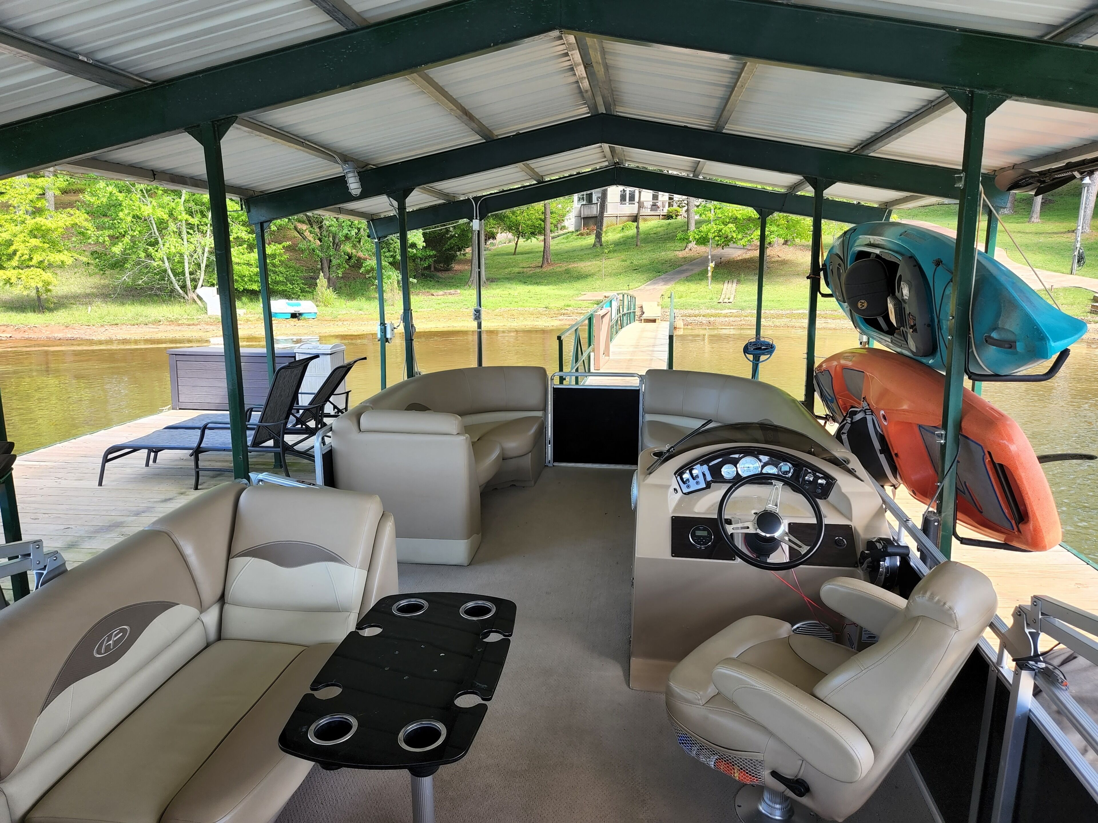A covered boat deck with seating, a steering wheel, and a kayak.