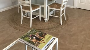 A dining area with a round table, four white chairs, a magazine on a small table, a horse painting on the wall, and a door. - Wellington Guest Suite (Wellington)