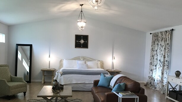 A spacious living room with a large bed, a brown sofa, a coffee table, and a chandelier. - Wellington Guest Suite (Wellington)