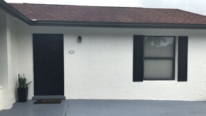 A white building with a black door, a window with shutters, and a welcome sign. - Wellington Guest Suite (Wellington)