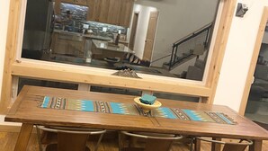 Un comedor con una amplia mesa de madera, cuatro sillas y un espejo grande sobre la mesa.