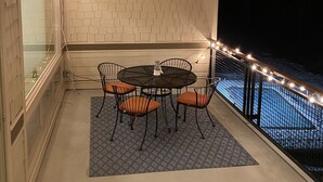 Un balcón con una mesa redonda y sillas, una alfombra estampada y luces colgantes.