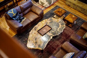 A brown leather sofa with a blanket, a marble coffee table, and matching ottomans in a cozy living room with a patterned rug and a stone fireplace. - Yellowstone Lodge: Sleeps 18 + Game Room + Loft (Broken Bow)