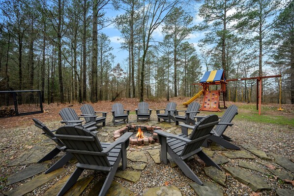A fire pit surrounded by Adirondack chairs in a forested area. - Yellowstone Lodge: Sleeps 18 + Game Room + Loft (Broken Bow)