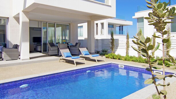 Un área de piscina moderna con sillones reclinables y una piscina de color azul cristalino.