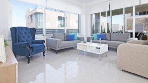 Una sala moderna con un sillón azul, sofás grises y una mesa de centro blanca.