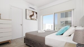 Un dormitorio moderno con cama, mesita de noche, lámpara, ventana con vistas y puerta.