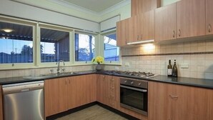 Eine moderne Küche mit Holzausstattung, einem Edelstahl-Geschirrspüler, einem Gasherd und einer gefliesten Spritzschutzwand.