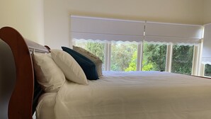 Ein Schlafzimmer mit Bett, Kissen, einem Fenster mit Blick auf Grünflächen und einem Holzkopfende.