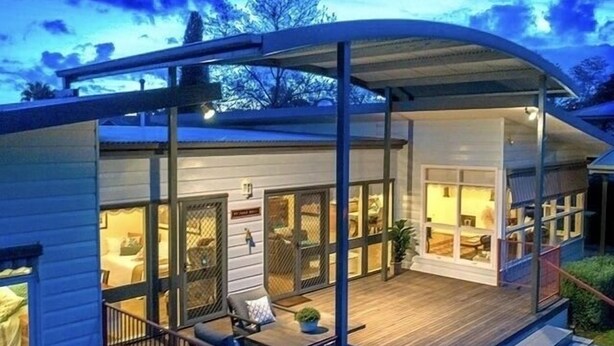 Ein modernes Haus mit einer überdachten Terrasse, großen Fenstern und einem Holzboden.