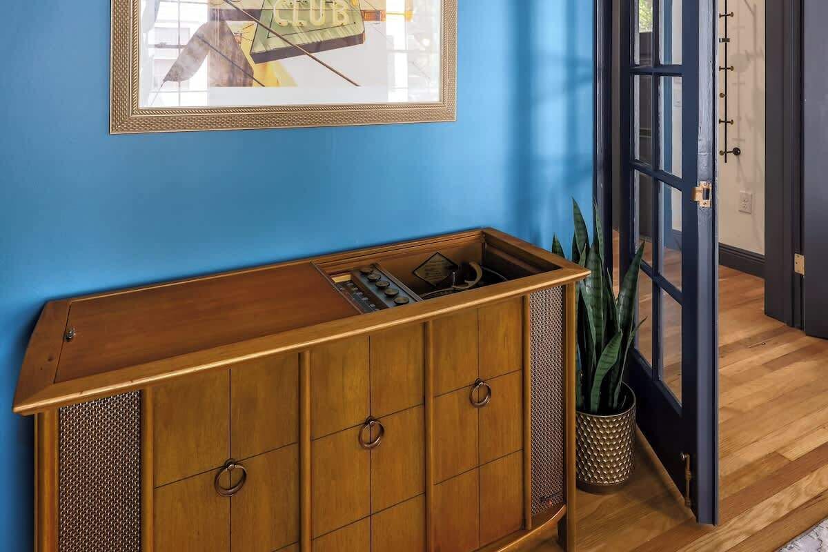 A wooden cabinet with a mesh panel and a framed picture on a blue wall.