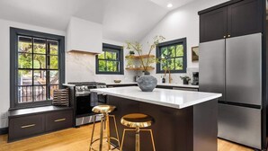 Una cocina moderna con una isla grande, armarios oscuros, electrodomésticos de acero inoxidable y vistas al exterior a través de amplias ventanas.
