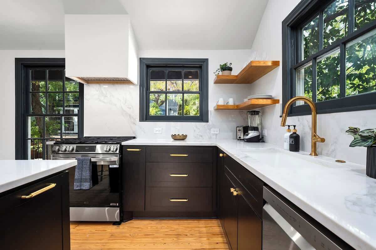 Une cuisine moderne avec des meubles de couleur sombre, un plan de travail blanc et une grande fenêtre.