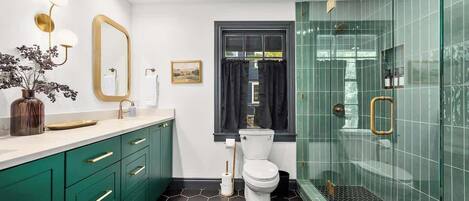 A modern bathroom with green cabinets, a white toilet, a glass shower enclosure, and a hexagonal floor pattern.