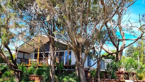 A modern house with a large deck, surrounded by mature trees and a well-maintained garden. - Stylish modern open‑plan beach house offering a warm, welcoming, home‑like vibe. (Manyana)