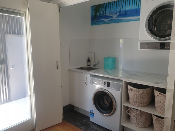 A laundry room with a washing machine, a sink, and a towel rack. - Stylish modern open‑plan beach house offering a warm, welcoming, home‑like vibe. (Manyana)