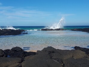 A rocky shoreline with clear blue water and waves crashing against the rocks. - Stylish modern open‑plan beach house offering a warm, welcoming, home‑like vibe. (Manyana)