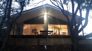 A modern house with a large glass window, a wooden deck, and a stone pillar. - Stylish modern open‑plan beach house offering a warm, welcoming, home‑like vibe. (Manyana)