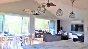 A spacious living area with a large marble island, dining area with white chairs, and a TV mounted on the wall. - Stylish modern open‑plan beach house offering a warm, welcoming, home‑like vibe. (Manyana)