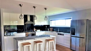 A modern kitchen with a central island, bar stools, a stainless steel refrigerator, and pendant lighting. - Stylish modern open‑plan beach house offering a warm, welcoming, home‑like vibe. (Manyana)