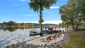 A lakeside deck with a gazebo, lounge chairs, and a dock with a boat.