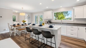 A modern kitchen with white cabinetry, a central island with bar stools, and a large window providing a view of the outdoors.