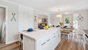 A modern kitchen with white cabinetry, a central island, and a dining area with a wooden table and chairs.
