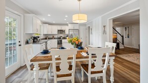 A modern kitchen with white cabinetry, a wooden dining table, and a hanging light fixture.