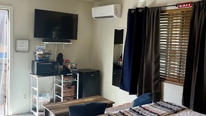 A hotel room with a bed, a desk with a computer, a ceiling fan, an air conditioner, a television, and a window with curtains. - Room with mountain views/hiking, private entrance & peaceful courtyard. (Phoenix)