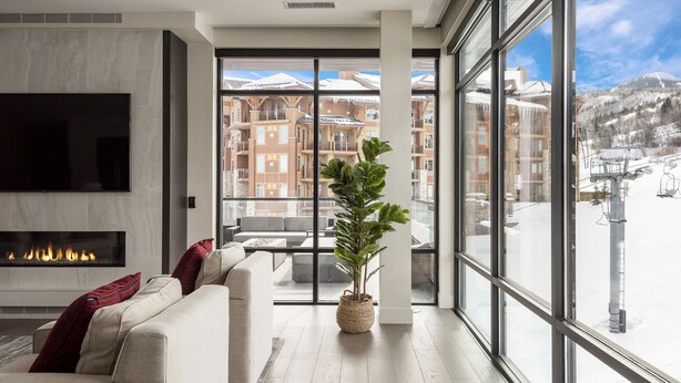 Un soggiorno moderno con camino, un'ampia finestra che offre vista su edifici innevati e una seggiovia.