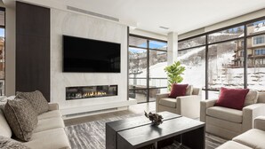 Un soggiorno moderno con camino, posti a sedere confortevoli, una TV a schermo piatto e ampie finestre che offrono vista su un paesaggio innevato.