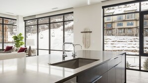 Una cucina moderna con una grande isola, lavello integrato e vista su un paesaggio innevato attraverso ampie finestre.