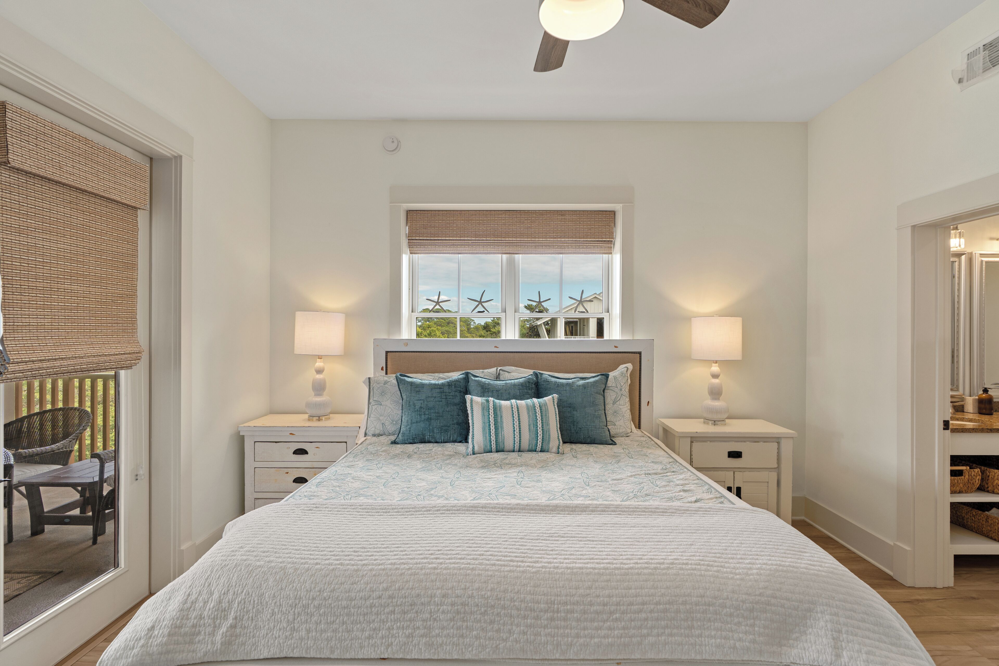A bedroom with a large bed, two bedside tables with lamps, a window with blinds, and a ceiling fan.