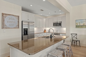 Una cocina moderna con armarios blancos, electrodomésticos de acero inoxidable y una isla de granito con taburetes.
