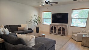 A modern living room with a sectional sofa, a coffee table, a TV on a wooden cabinet, and a potted plant. - Zion Canyon Retreat - Private Pool & Pickleball Court, Spacious, Clean & FUN!!! (La Verkin)
