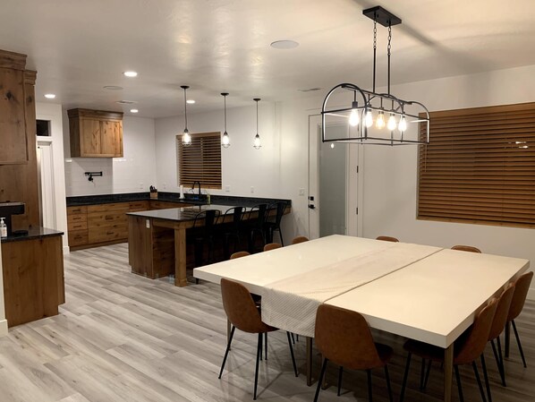A modern kitchen with wooden cabinets, a central island, and a dining area with a white table and brown chairs.