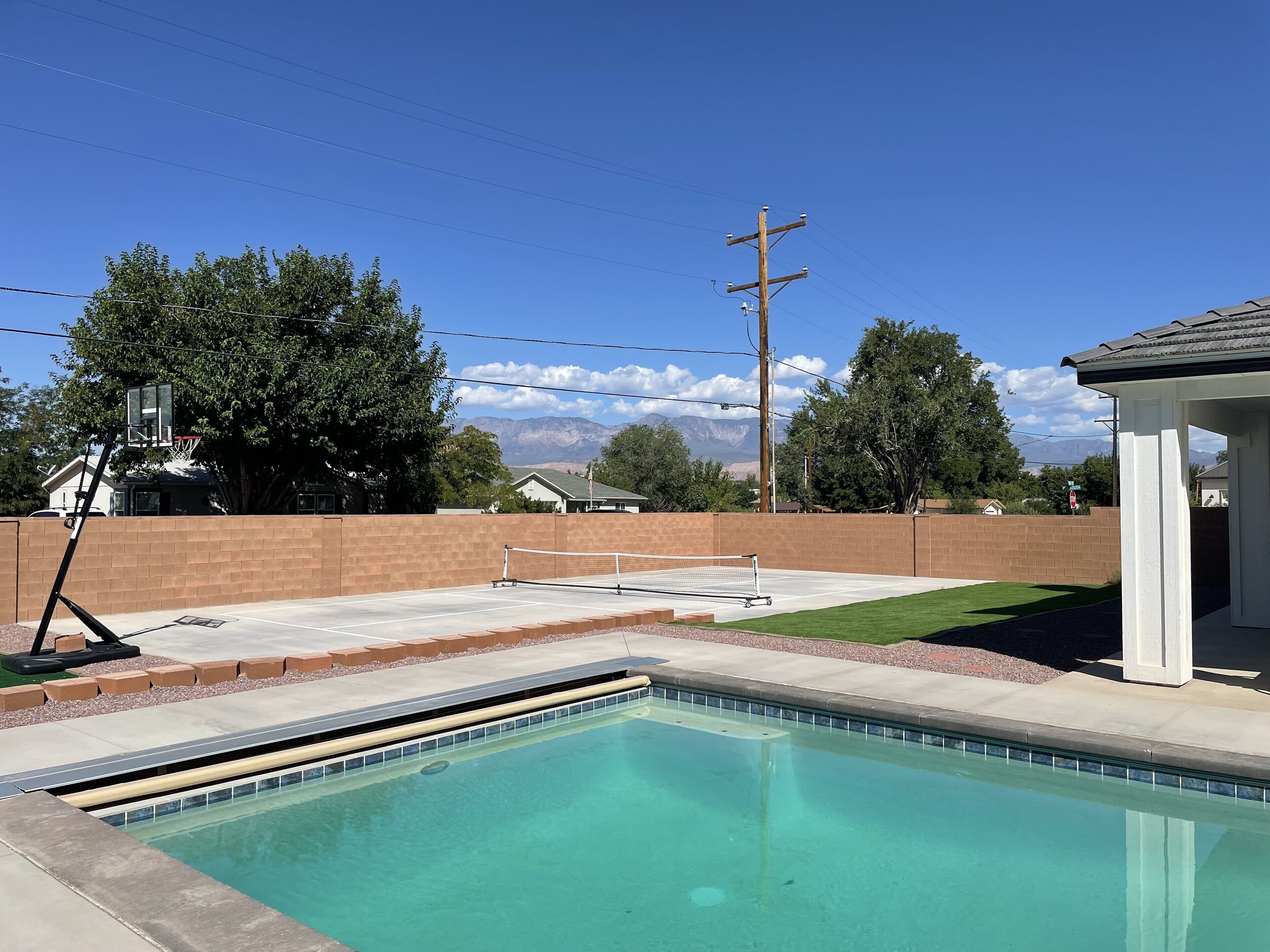 A swimming pool with a basketball court and a tennis court in the background.