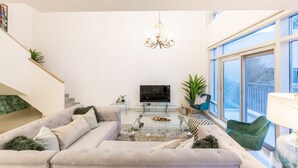 Ein modernes Wohnzimmer mit einer großen Couch, einem Glastisch, einem Fernseher und einer Treppe mit einer Pflanze.